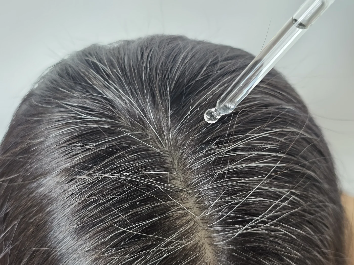 A dropper applying Crowned serum directly along the part line